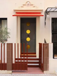A traditional house with a white exterior, a red door, and a window, set in a natural outdoor setting with a potted plant in the foreground, lit by natural sunlight