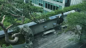 一位女性坐在一張長椅上，在一個現代化的頂樓露台上，旁邊有桌子和椅子，種植了幾盆植物，令人放鬆和親切的城市環境中