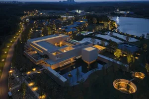 A nighttime scene of a large concrete building with a pool in front, illuminated by artificial lighting, creating a serene and inviting atmosphere
