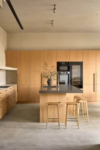 Warm and inviting kitchen with wooden cabinets and countertops, a center island with a sink, refrigerator, and oven, and three stools for seating