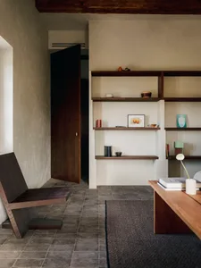 A well-lit living room with a wooden floor, a bookshelf, a chair, a table, and a vase, creating a warm and inviting atmosphere