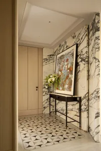 A dimly lit room with a black and white marble floor, a marble-framed doorway, and a painting on the wall, with a vase and flowers on a table