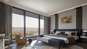 A modern bedroom with a bed, couch, and chair, featuring a large window and a predominantly white color scheme, with wood and leather furniture