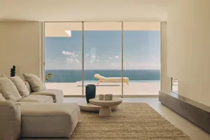 Coastal living room with a modern sofa, armchair, coffee table, and decorative items, set against a large window with an ocean view