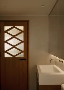 A modern bathroom with a white sink, glass window, and metal door, set against a well-lit background