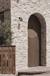 A doorway with a wooden door and stone wall, adorned with a light fixture, set against a building facade