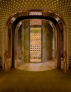 A modern hallway with a gold-framed doorway, patterned wallpaper, and warm lighting