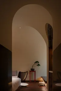 Cozy living area with a red table, a potted plant, a couch, and a chair, surrounded by white walls and a vase