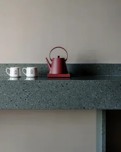 A kitchen counter with a red teapot and two white cups, set against a marble surface in a warm and inviting space