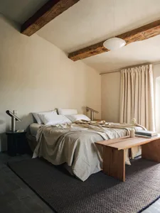 Cozy bedroom with a wooden floor, a white wall, and a dimly lit bed with a blanket and pillows