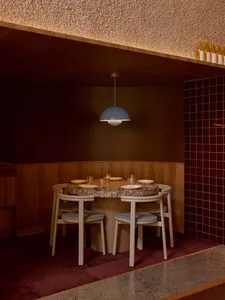 Dining room with a wooden floor, a modern dining table, chairs, and wine glasses, lit by a hanging light fixture in a dim, cozy atmosphere