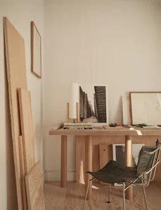 A cozy home office with a wooden desk, chair, and various items, including a book, cup, and vase, in a living space with a focus on the desk area