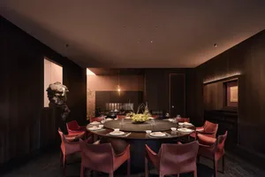 Dining room with a round table, wooden floor, and natural light from a window, set with plates, wine glasses, and vases