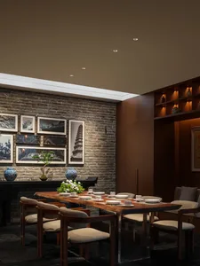 A warm and inviting dining room with a wooden table, brick wall, and potted plant, set with plates, bowls, and cups