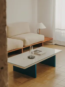 A modern living room with a blue sofa, glass coffee table, and neutral color palette, featuring clean lines and simple design