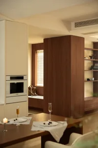 Modern living room with a wooden floor, white walls, a kitchen area, dining table, potted plant, and bookshelf
