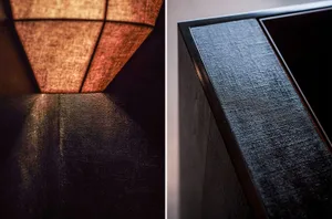 A dimly lit dining room with a wooden floor, a black table, a lamp, and comfortable seating
