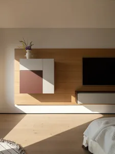 A modern living room with a wooden floor and white walls, featuring a flat-screen TV, cabinet, and vase with flowers, with natural light and a clean aesthetic