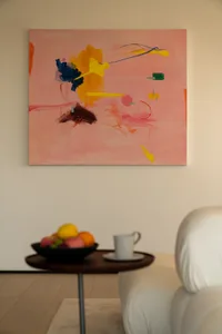 A warm and inviting room with a large abstract painting on the wall, a couch, dining table, and fruit and a cup on the table