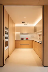 A modern kitchen with wooden cabinets, white countertops, a sink, oven, and microwave, lit by bright overhead lighting