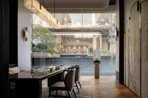 A modern restaurant with a large window, a dining table, chairs, and various table settings, set in a well-lit space with natural light