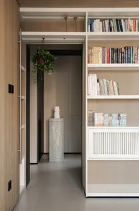 Cozy living area with a bookshelf filled with books, a potted plant, and a doorway, set against a neutral background