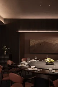 Cozy dining room with a round table set for a meal, surrounded by chairs, on a wooden floor, in a brown color scheme, with dim lighting
