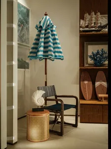 A modern living room with a blue and white striped umbrella hanging from the ceiling, a chair, table, and surfboard, with a warm and natural feel from the wood materials and well-lit atmosphere