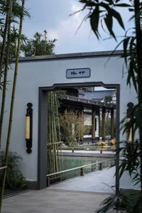 A traditional building with a large entrance featuring bamboo elements, set in an outdoor environment with a nearby pond