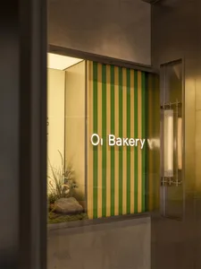 一間充滿光線的面包店，綠、黃條紋的窗口展示和一塊刻有 "Oi Bakery" 的招牌