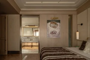 A well-lit bedroom with a bed, chair, and painting, featuring wood and fabric materials, creating a warm and inviting atmosphere
