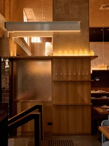 Warm and inviting restaurant with wooden walls, floors, and furniture, featuring a bar with wine glasses and bottles, and natural lighting