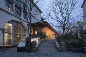 A stone staircase leads up to a brick building in a serene courtyard setting with a bench at the base of the stairs