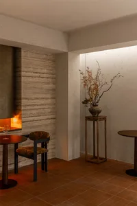A warm and inviting dining area with a wooden table, chairs, and a vase with flowers, surrounded by stone walls and soft warm lighting