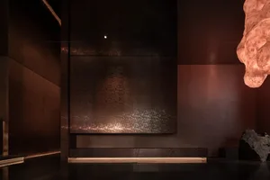 Dimly lit room with a brown wall, a bench, and a sense of depth from a low-angle perspective