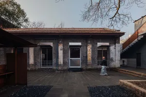 A woman walks towards a brick building with a tiled roof, set in an outdoor scene