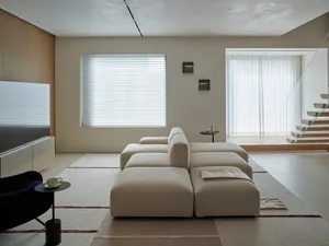A modern living room with a white couch and chair, a TV on the left, and a coffee table in the center, set in a well-lit space with a clean design