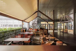 An inviting outdoor dining area with a wooden floor, brown tables, black chairs, and a shaded canopy