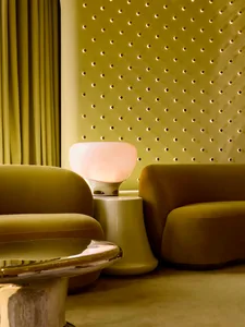 A cozy living room with a green couch and chair, a pink lamp, and a well-lit atmosphere