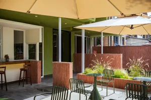 A modern outdoor dining area with a green and yellow color scheme, featuring multiple tables and chairs, umbrellas, and well-lit surroundings
