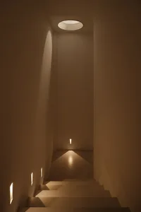 A bright and inviting hallway with a white concrete wall and a light shining down the center, illuminating the space