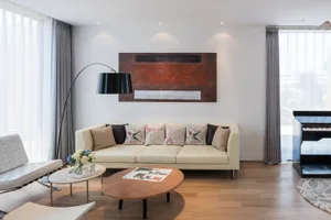 Cozy living room with a brown couch, chair, coffee table, and vase with flowers, set against a dimly lit background with a painting on the wall