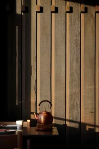 A tea kettle and cup sit on a table next to a wooden wall in a warm and inviting indoor setting