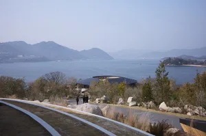 A large building near a body of water features a central circular structure with people walking around, blending architectural and natural elements