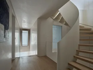 A modern staircase with a wooden floor and a glass railing, located in a well-lit hallway with a nearby window