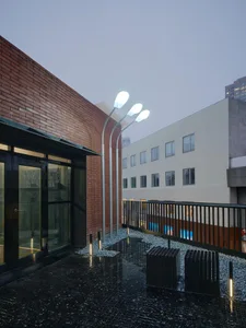 Exterior photo of a modern building with a brick facade, a wooden balcony, and a stone patio, set in a dimly lit atmosphere