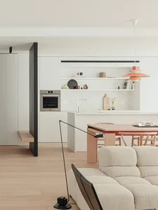 A modern kitchen and living space with a white oven, sink, and dining table, a couch and chair in the living room, and natural light from the windows