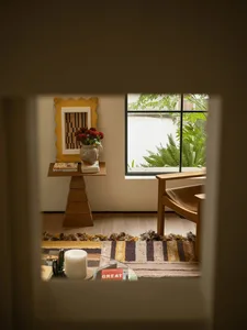 Cozy living room with a wooden floor, a couch, chair, and dining table, featuring natural light and a vase with flowers