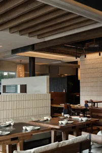 A modern restaurant interior with wood paneling, natural lighting, and a variety of materials, featuring tables, chairs, and dining area