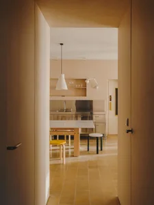 A modern kitchen with a wooden floor, dining table, chairs, and natural light from windows